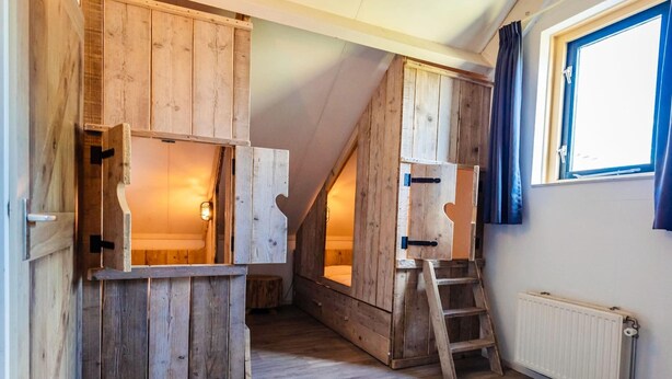 Ein Zimmer mit Holzwänden, einer Leiter und einem Fenster.