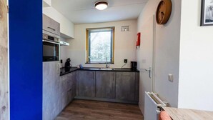 Eine kleine Küche mit Backofen, einem Fenster mit Jalousien, einer Uhr und einer Heizung.
