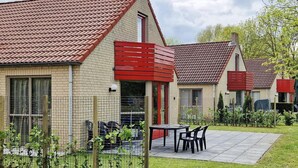 Eine Reihe moderner Häuser mit roten Akzenten, einer gepflasterten Terrasse und einem eingezäunten Garten.