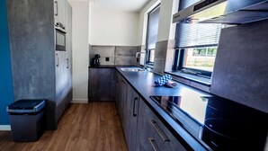A modern kitchen with dark cabinetry, a stainless steel sink, and a window with blinds.