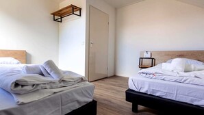 A hotel room with two beds, a wooden floor, a wardrobe, and a small bedside table with a lamp.