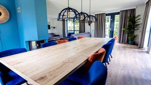 A modern dining area with a long wooden table, blue upholstered chairs, and a hanging light fixture.