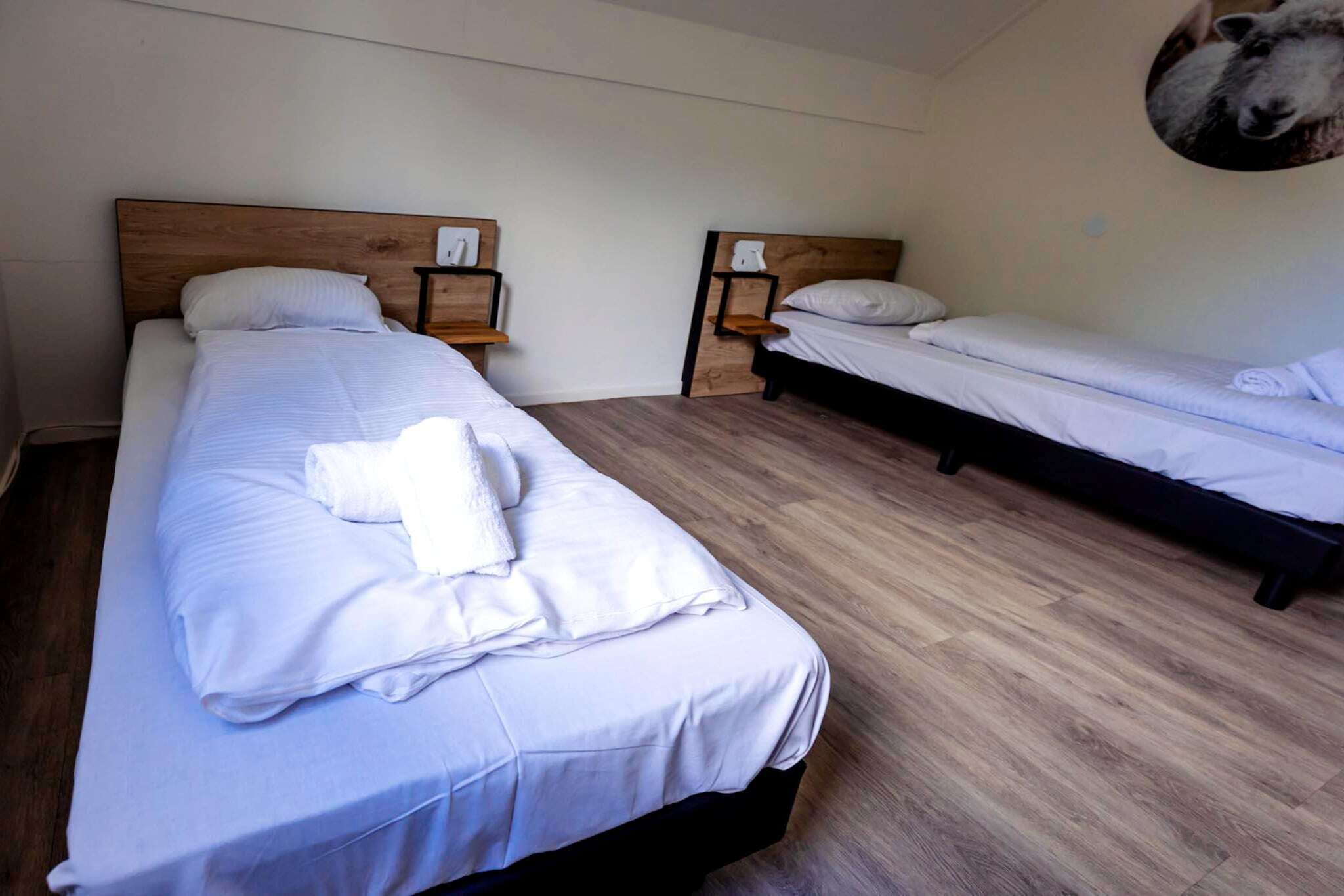 Quarto de hotel com duas camas, cabeceiras de madeira, mesas de cabeceira e prateleira na parede.