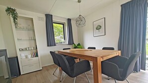Un comedor moderno con una mesa de madera, sillas negras, un mueble blanco con estantes de vidrio y una ventana con cortinas.