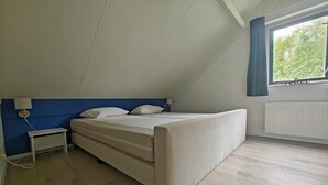 Un dormitorio con cama, mesita de noche y ventana con cortinas.