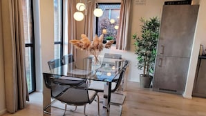 A modern kitchen with a glass dining table, chairs, a refrigerator, and a potted plant.