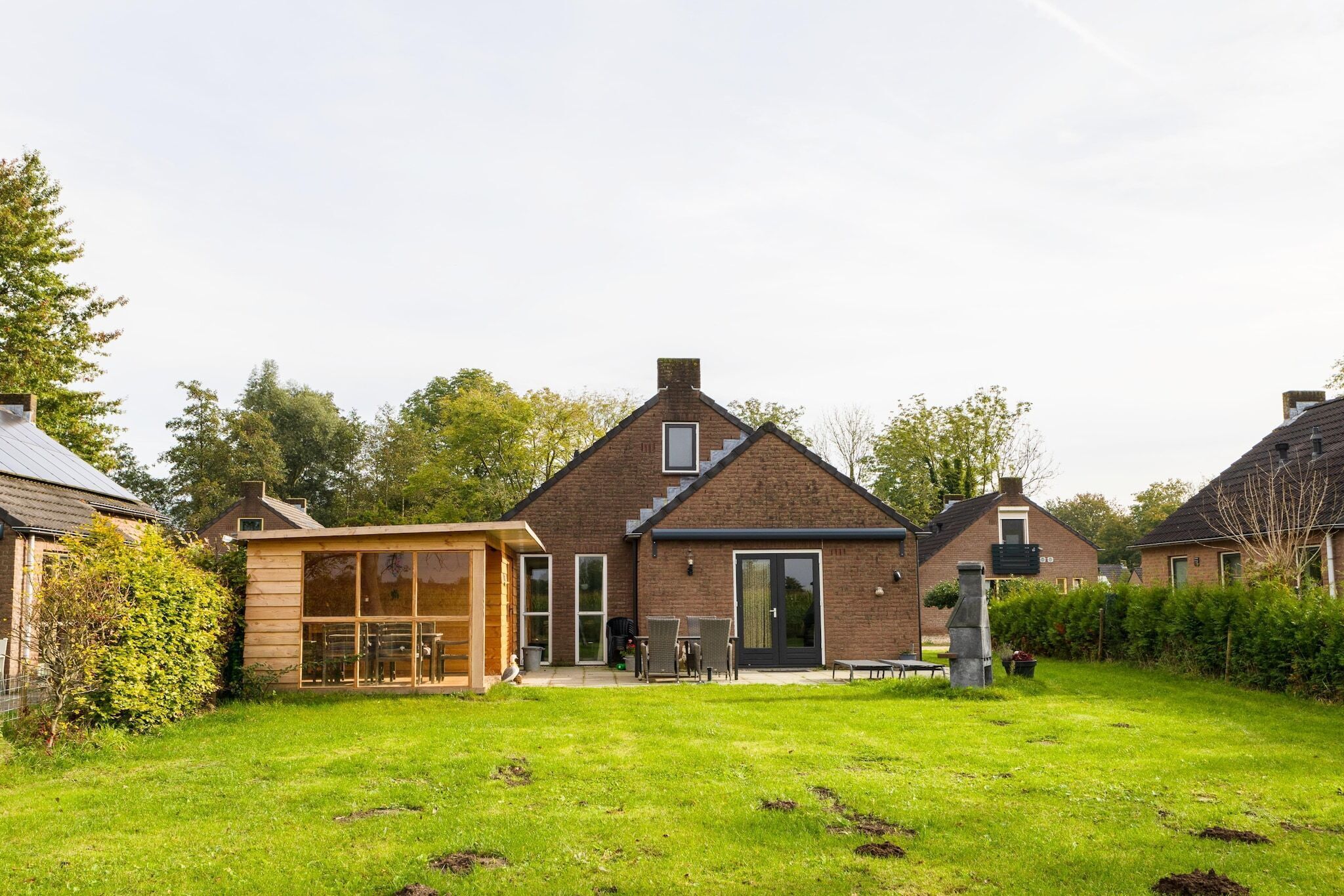 Een modern huis met een bakstenen gevel, een houten terras en een verzorgd gazon.
