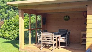 A wooden deck with a table and chairs, a dartboard, and a small shelf.