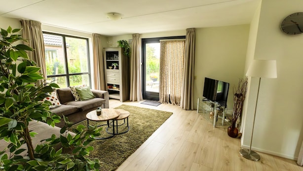 A living room with a sofa, coffee table, and a TV. There is a bookshelf and a plant.