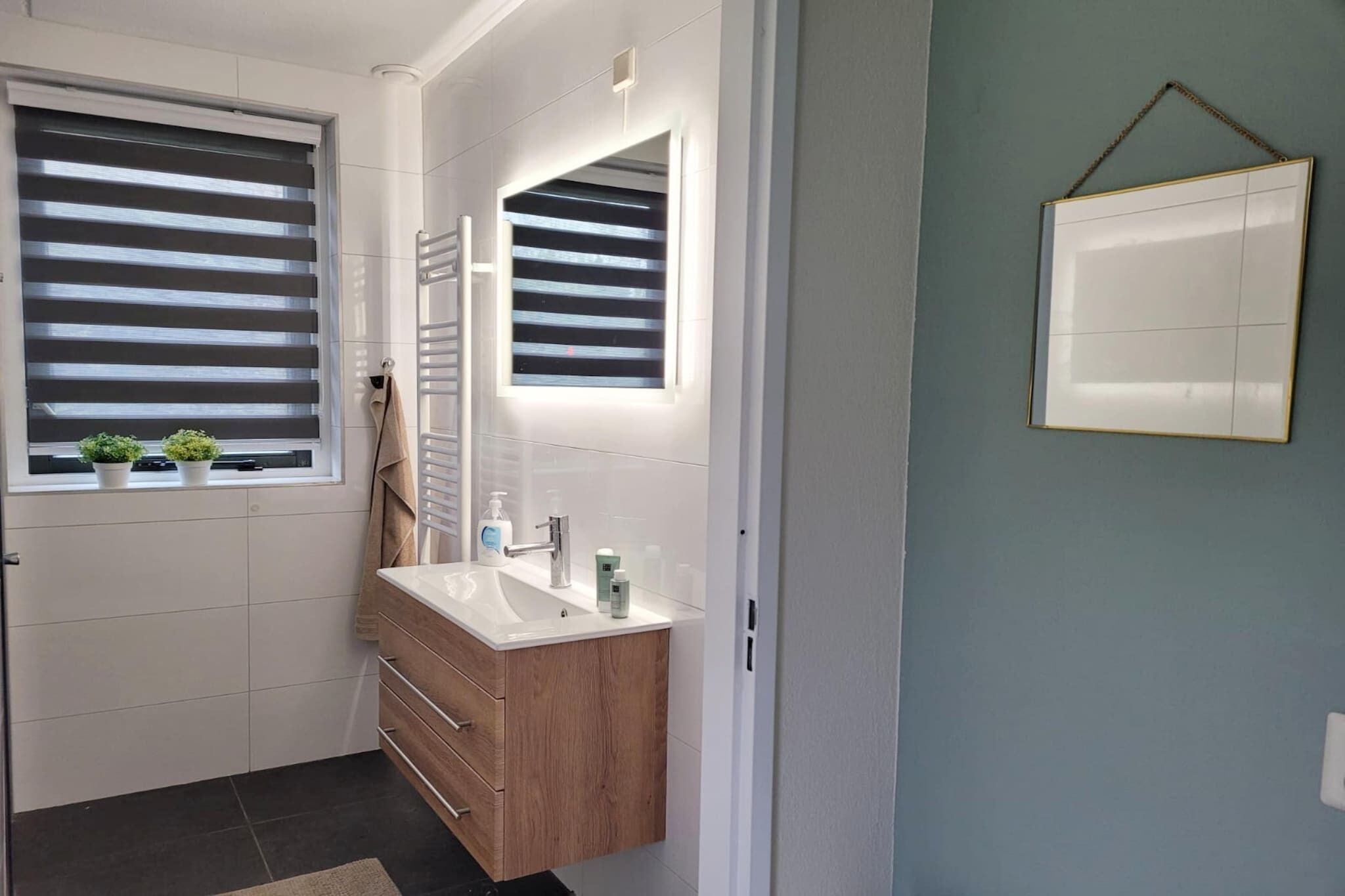 A bathroom with a sink, mirror, towel rack, and potted plants.