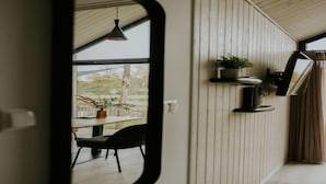A room with wooden paneling, a dining area with a table and chairs, and a window with a view of trees. - Charming Tiny House Getaway with Terrace. (Balkbrug)