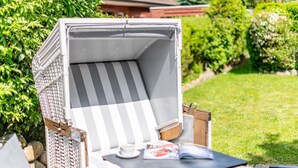 Un espace extérieur aménagé avec des meubles en osier, comprenant un fauteuil rembourré et une petite table, le tout entouré de verdure.
