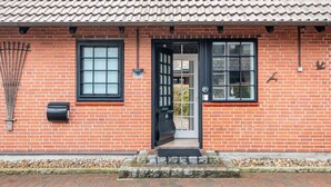 Un bâtiment en briques rouges, avec un toit recouvert de tuiles, une porte noire et une fenêtre à carreaux.