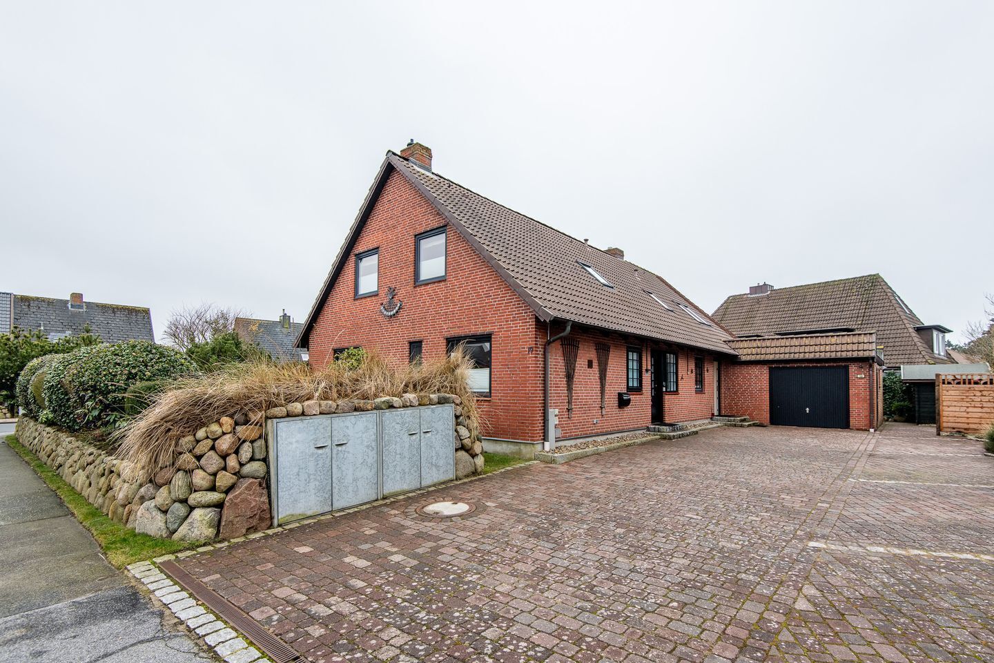 A red brick house with a garage, stone wall, and a paved driveway.