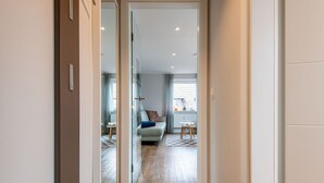Un couloir étroit mène à un espace de vie comprenant un canapé, une petite table et une fenêtre avec des rideaux.