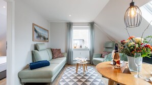 Un salon moderne avec un canapé, une table à manger agrémentée d’un vase de fleurs et une vue sur la ville grâce à de grandes fenêtres.
