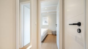 A hallway leading to a bedroom with a bed, a small stool, and a framed picture on the wall. - Strandbude Sylt Westerland - House Apenrader Straße (Sylt)