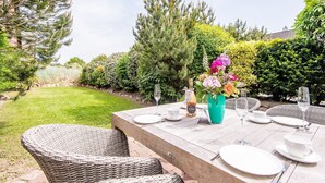 An outdoor dining area with a table set for four, surrounded by lush greenery and a well-maintained lawn. - Strandbude Sylt Westerland - House Apenrader Straße (Sylt)