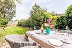 An outdoor dining area with a table set for four, surrounded by lush greenery and a well-maintained lawn.