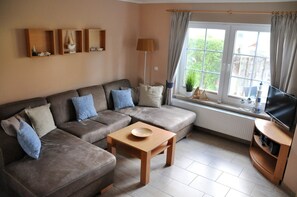 A living room with a sectional sofa, a wooden coffee table, a TV on a stand, and a window with curtains.