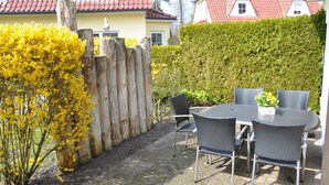 Une terrasse extérieure avec une table ronde et quatre chaises, entourée d’une clôture en bois et d’une haie.