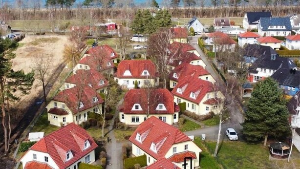 Un quartier résidentiel avec des maisons aux toits rouges, une vue dégagée sur la mer et une route asphaltée.