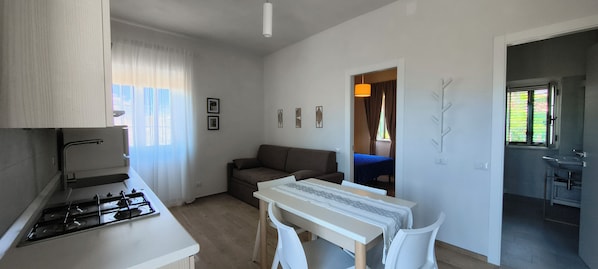 Cocina compacta con estufa a gas, una mesa de comedor con sillas, un sofá y una pequeña mesa con mantel azul.