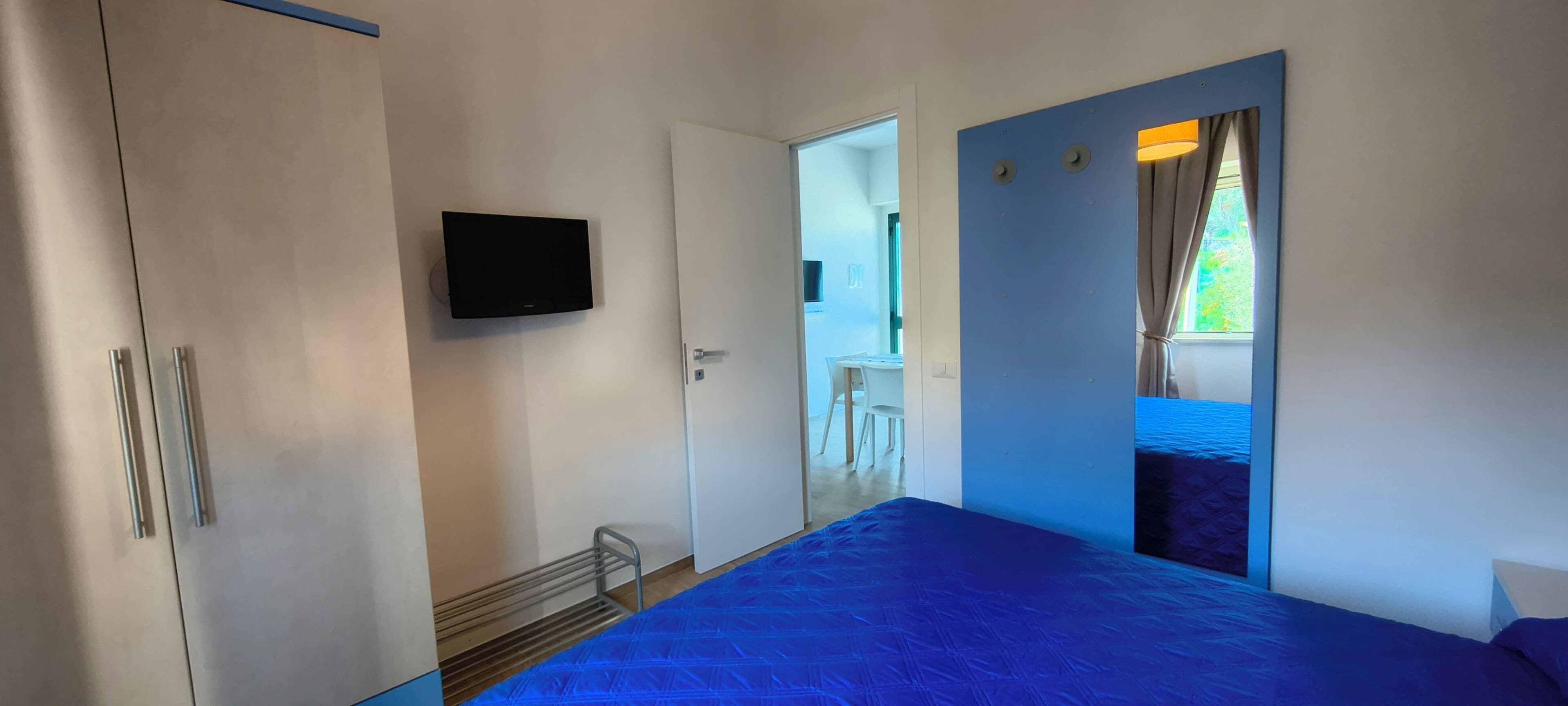 A bedroom with a bed, a TV mounted on the wall, and a door leading to a balcony.