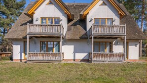 Una casa de dos pisos con techo de paja, balcones de madera y fachada blanca.