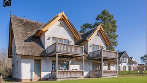 A two-story chalet with a thatched roof, wooden balconies, and a well-maintained lawn. - Modern vacation apartment with terrace & garden - relaxation on the Achterwasser - Loddin (Loddin)