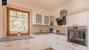 A modern kitchen with white cabinets, a built-in oven, and a window with a view of trees. - Modern vacation apartment with sauna & garden - close to nature and comfortable on Usedom - (Loddin)