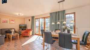 A spacious living room with a sofa, a TV, and a dining area with chairs and a table. - Modern vacation apartment with sauna & garden - close to nature and comfortable on Usedom - (Loddin)