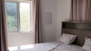 A neatly made bed with a headboard, a window with curtains, and a view of greenery outside. - Peaceful Willemstad Getaway - Entire Apartment for Rent (Willemstad)