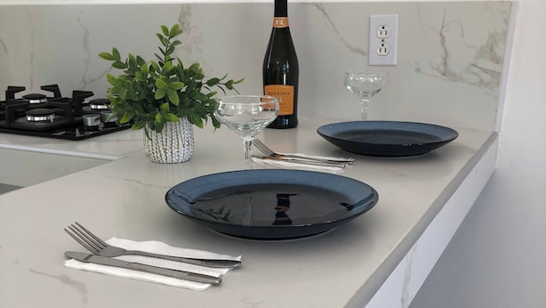 A kitchen counter with a bottle of wine, a glass, a potted plant, and a blue plate. - Peaceful Willemstad Getaway - Entire Apartment for Rent (Willemstad)