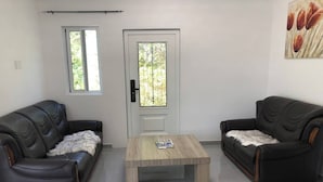 A living room with two black leather sofas, a wooden coffee table, and a door with a window. - Peaceful Willemstad Getaway - Entire Apartment for Rent (Willemstad)