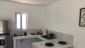 A compact kitchen with a built-in stove, a sink, and a window above it. There is a refrigerator and a coffee maker on the counter. - Peaceful Willemstad Getaway - Entire Apartment for Rent (Willemstad)