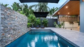 A modern outdoor pool area with stone walls, lounge chairs, and a pergola. - Casa Ponta | Port Douglas (PORT DOUGLAS)
