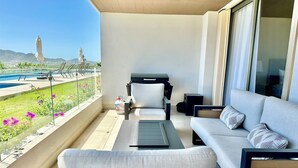 Un balcone con divano, sedie, tavolo e barbecue. Sullo sfondo, una piscina e montagne.