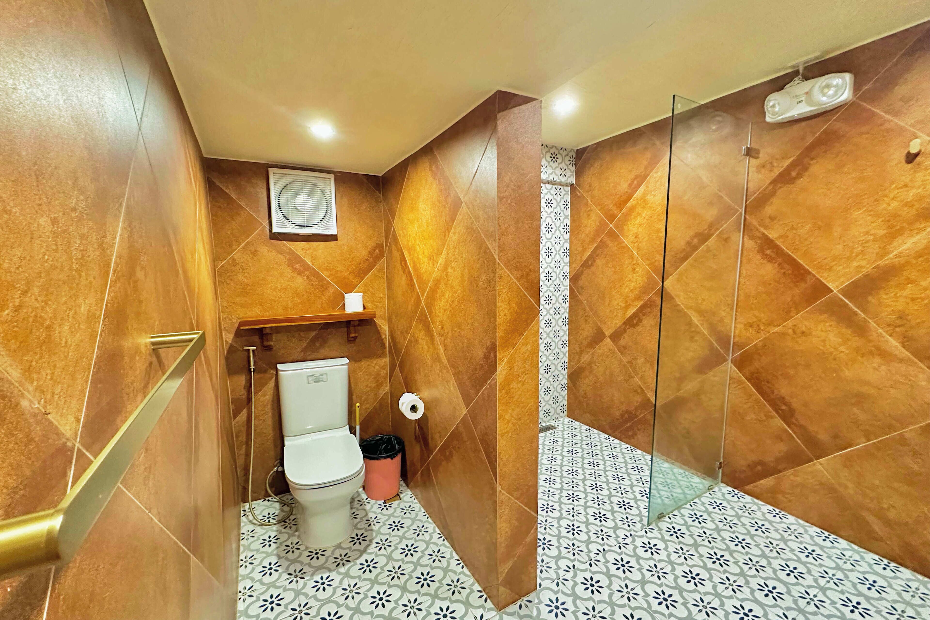 Une salle de bain équipée de toilettes, d’une poubelle, d’un espace douche et de carreaux de sol à motifs.