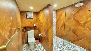 Une salle de bain équipée de toilettes, d’une poubelle, d’un espace douche et de carreaux de sol à motifs.