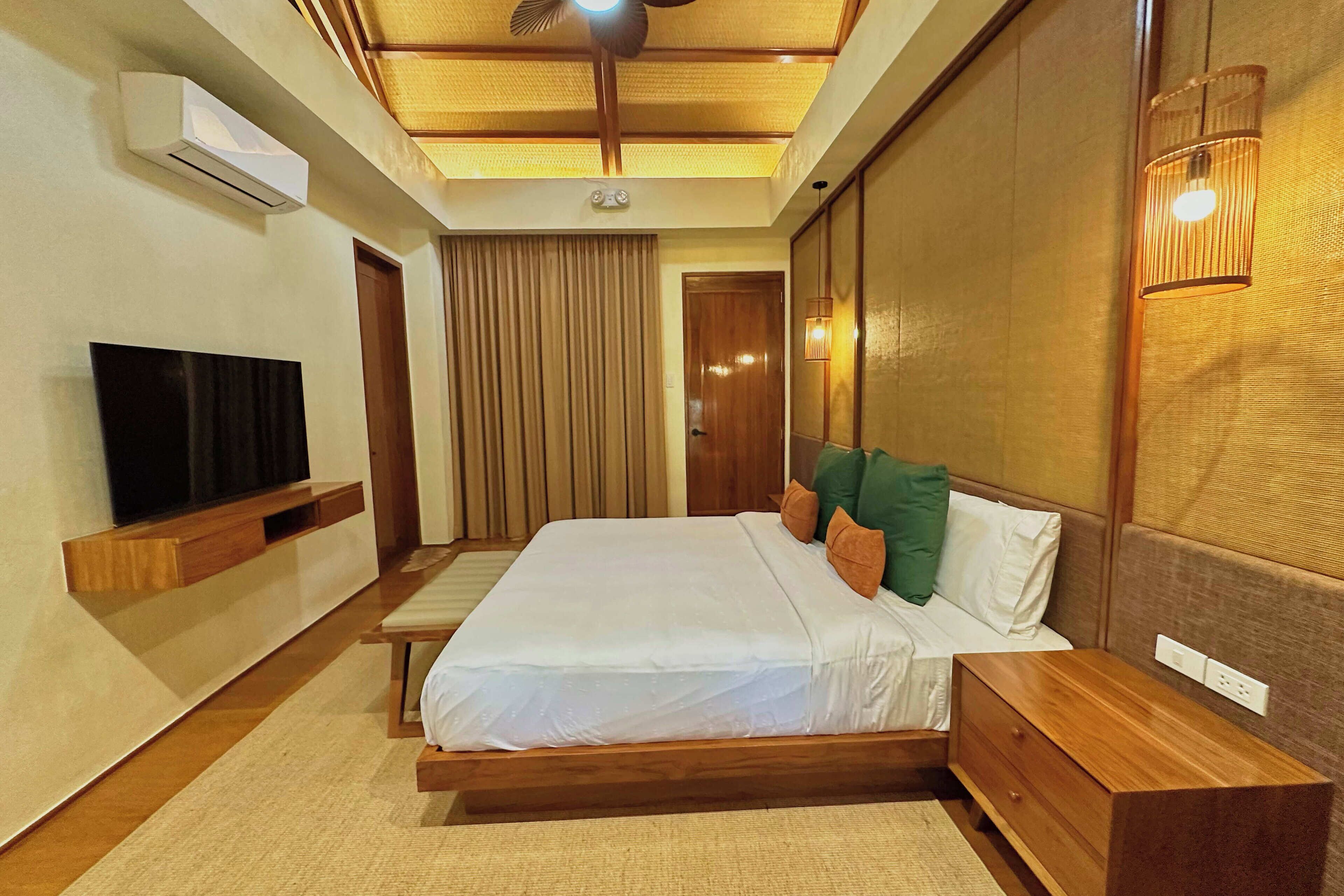 A hotel room with a bed, bedside table, TV, and a ceiling fan.