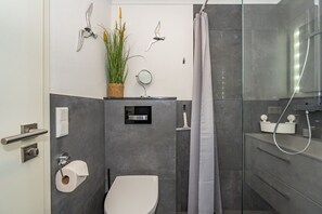 A modern bathroom with a toilet, shower, and a small sink area. - Dünenkoje App. 205 - Modern vacation apartment on Sylt with covered balcony and (Sylt)