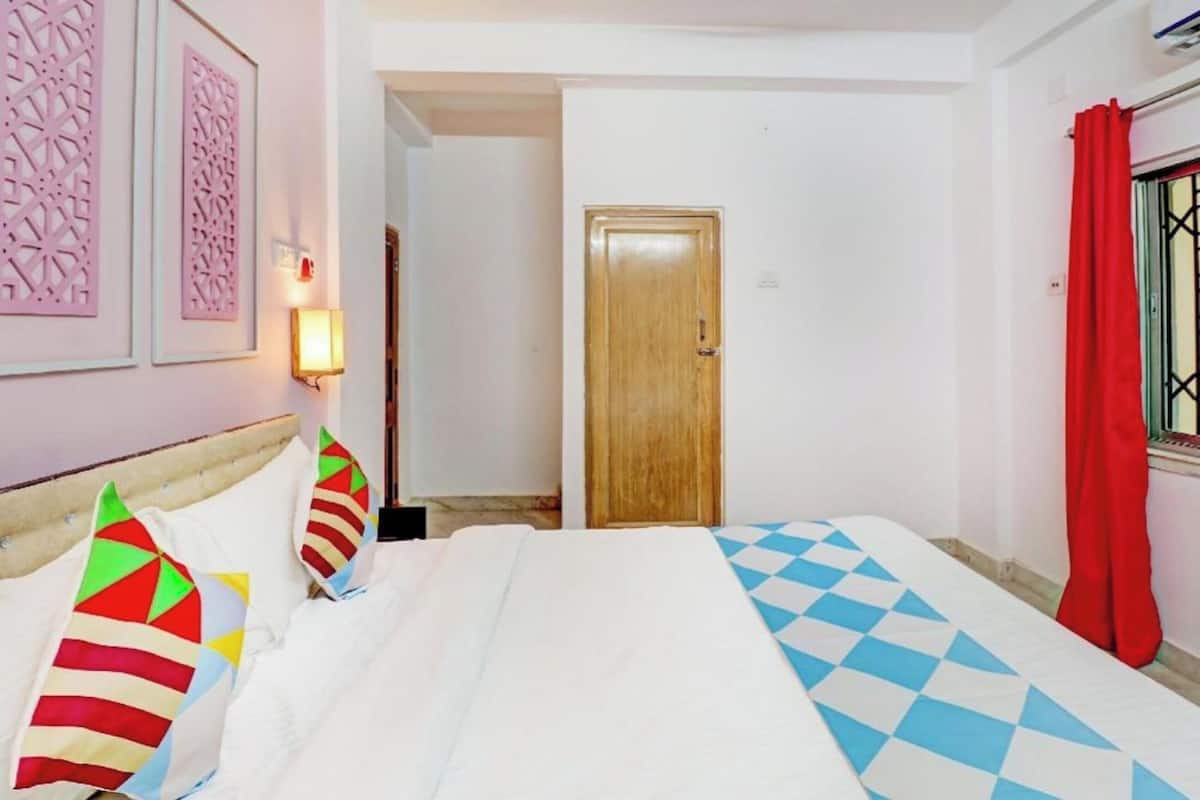 Ein Hotelzimmer mit einem Bett, einer Holztür, einer Wandlampe und einem Fenster mit rotem Vorhang.