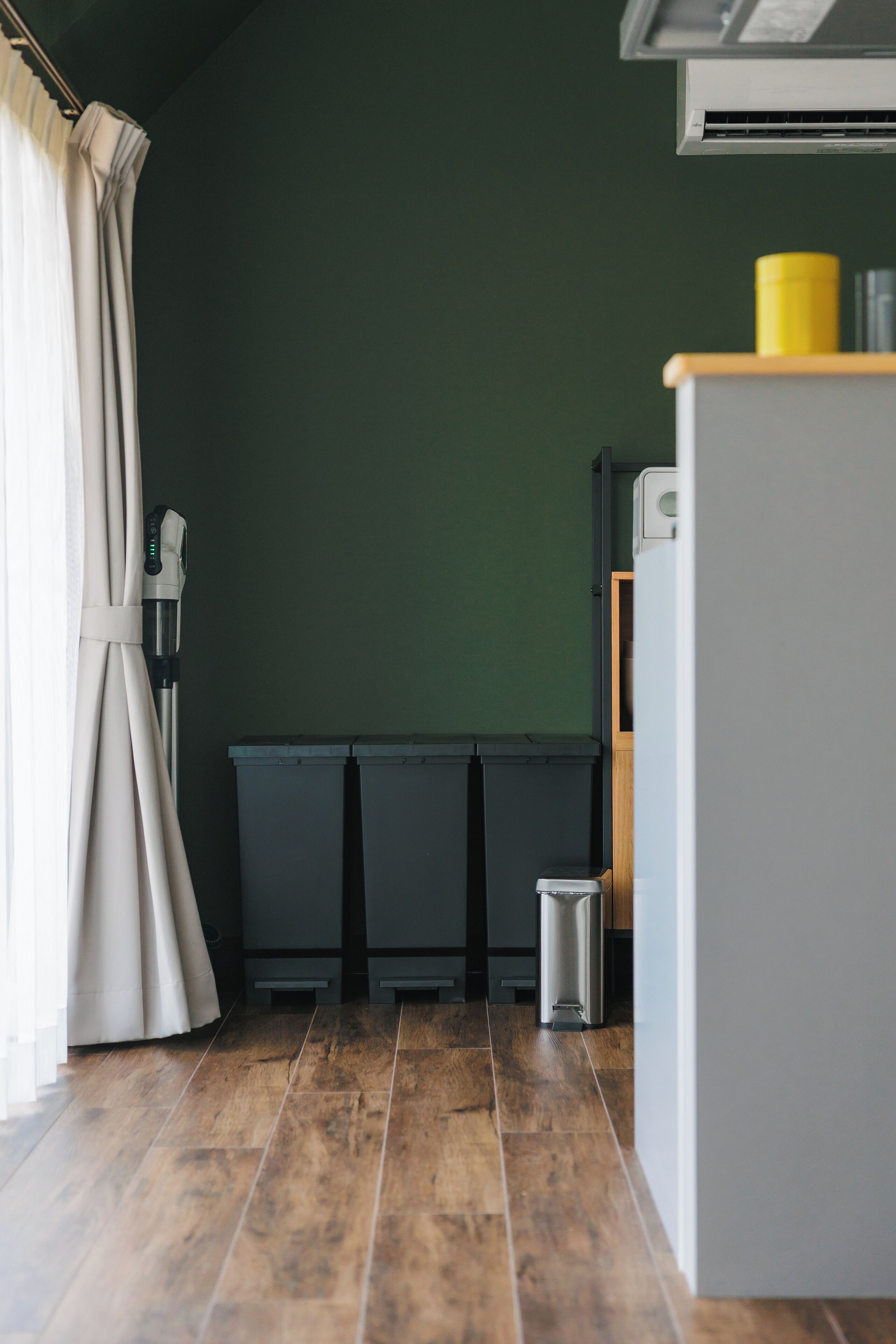 A kitchen with a green wall, a white refrigerator, and a trash bin.