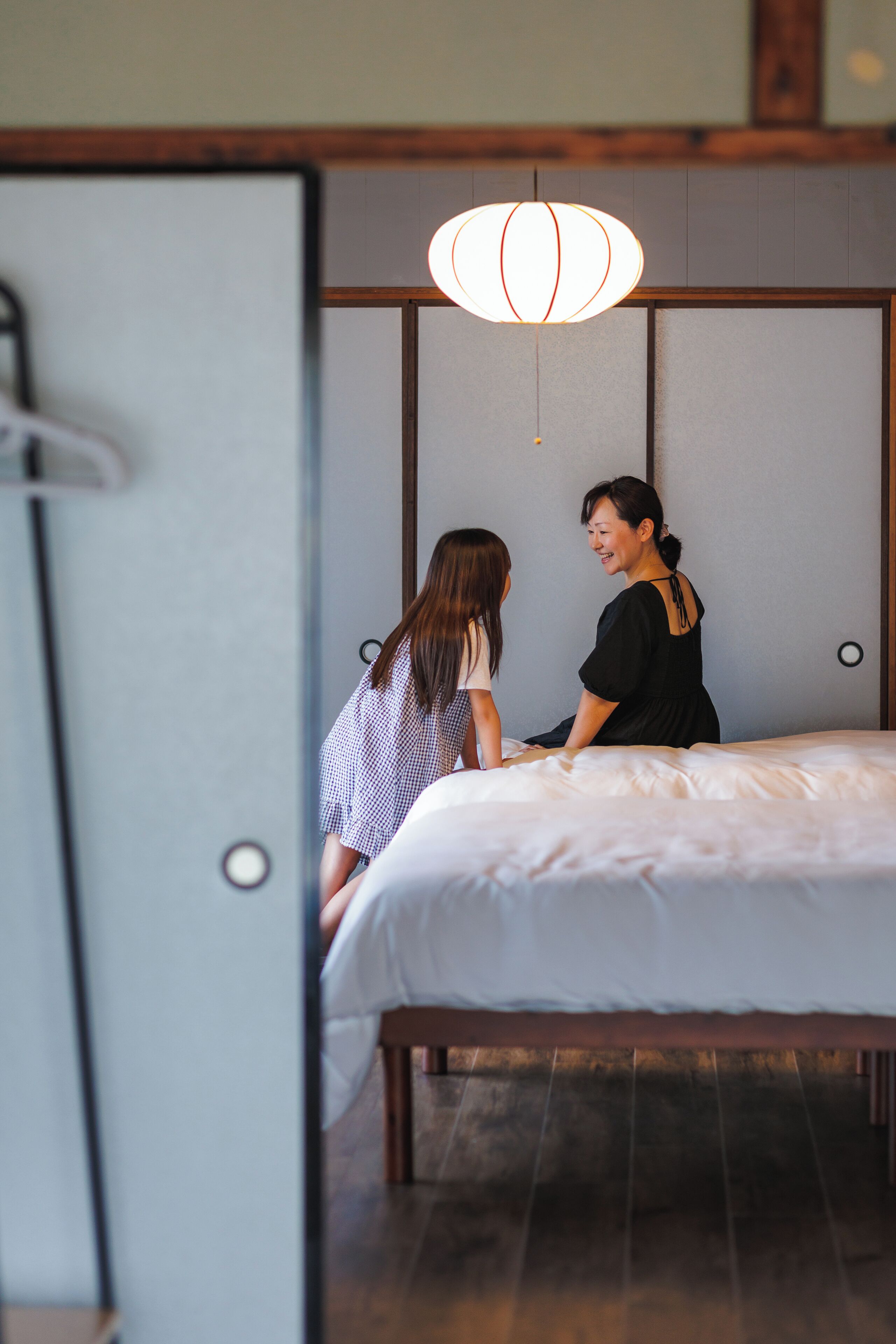 A room with a bed, a hanging light fixture, and a wooden floor.
