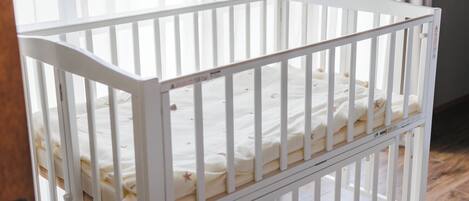 Una cuna blanca con un colchón blanco y suelo de madera.