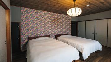 A room with two beds, wooden flooring, a floral wallpaper, and a ceiling light fixture.