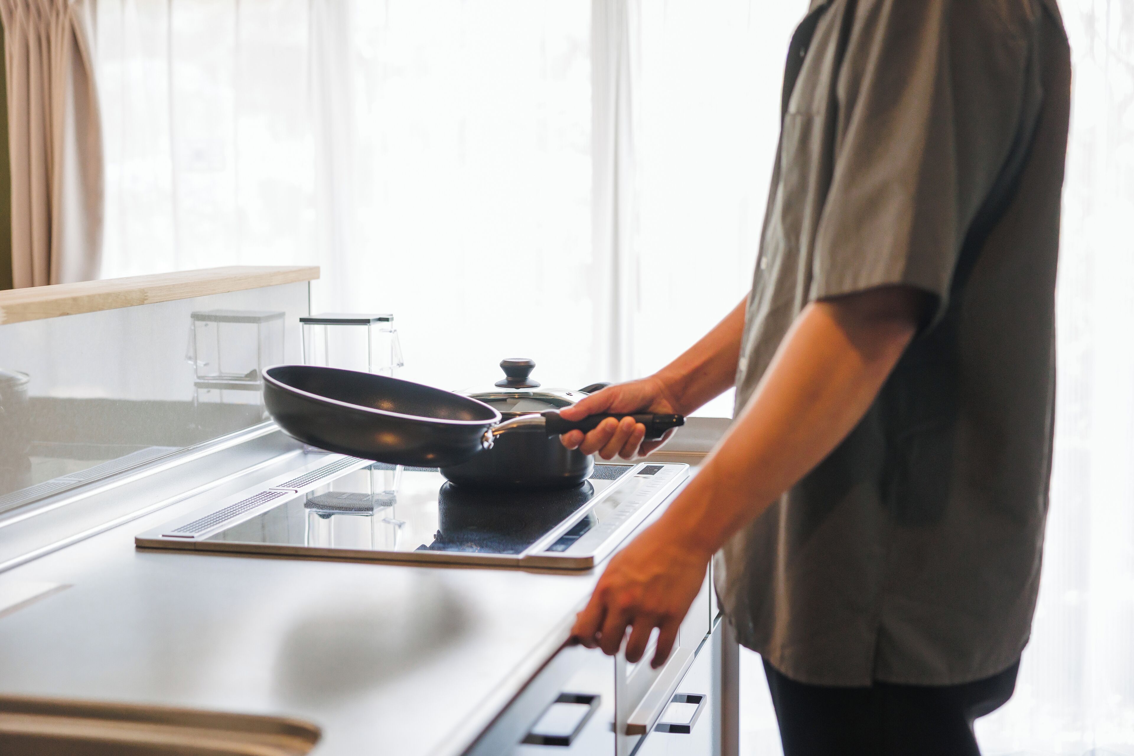 Une personne cuisine sur une plaque de cuisson à induction dans une cuisine moderne, avec une fenêtre en arrière-plan.