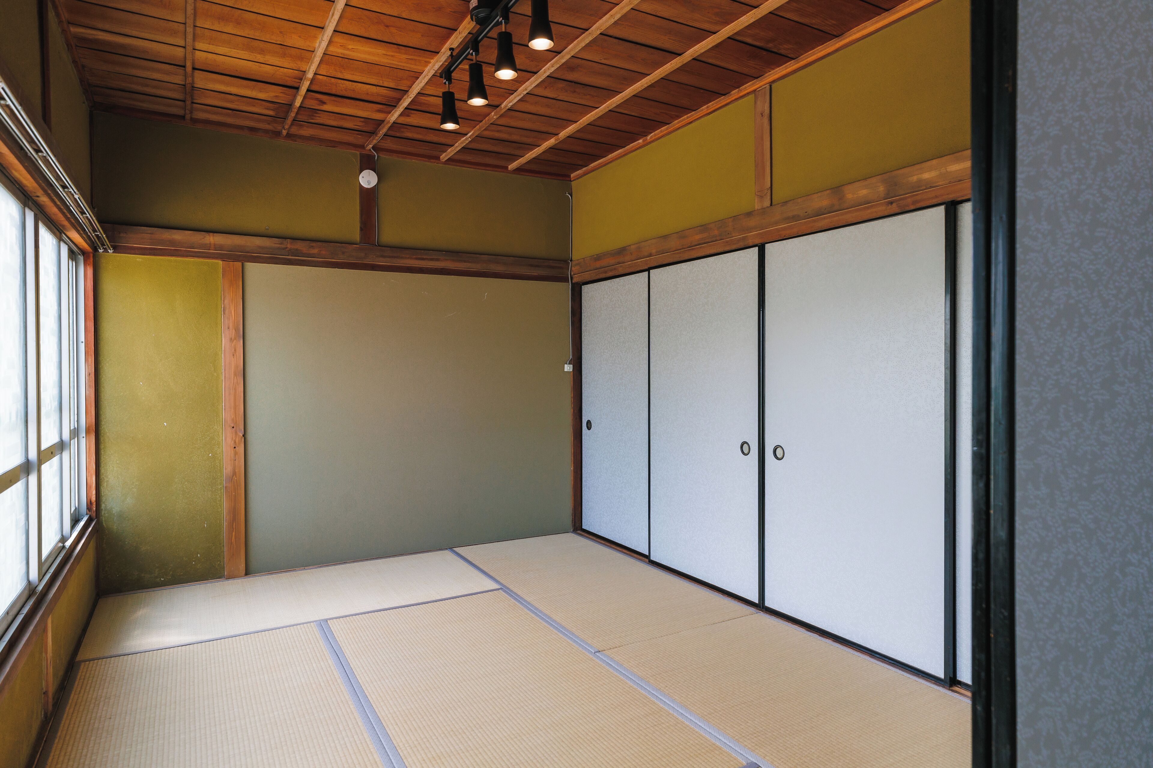 A traditional Japanese room with tatami flooring, sliding doors, and a wooden ceiling.