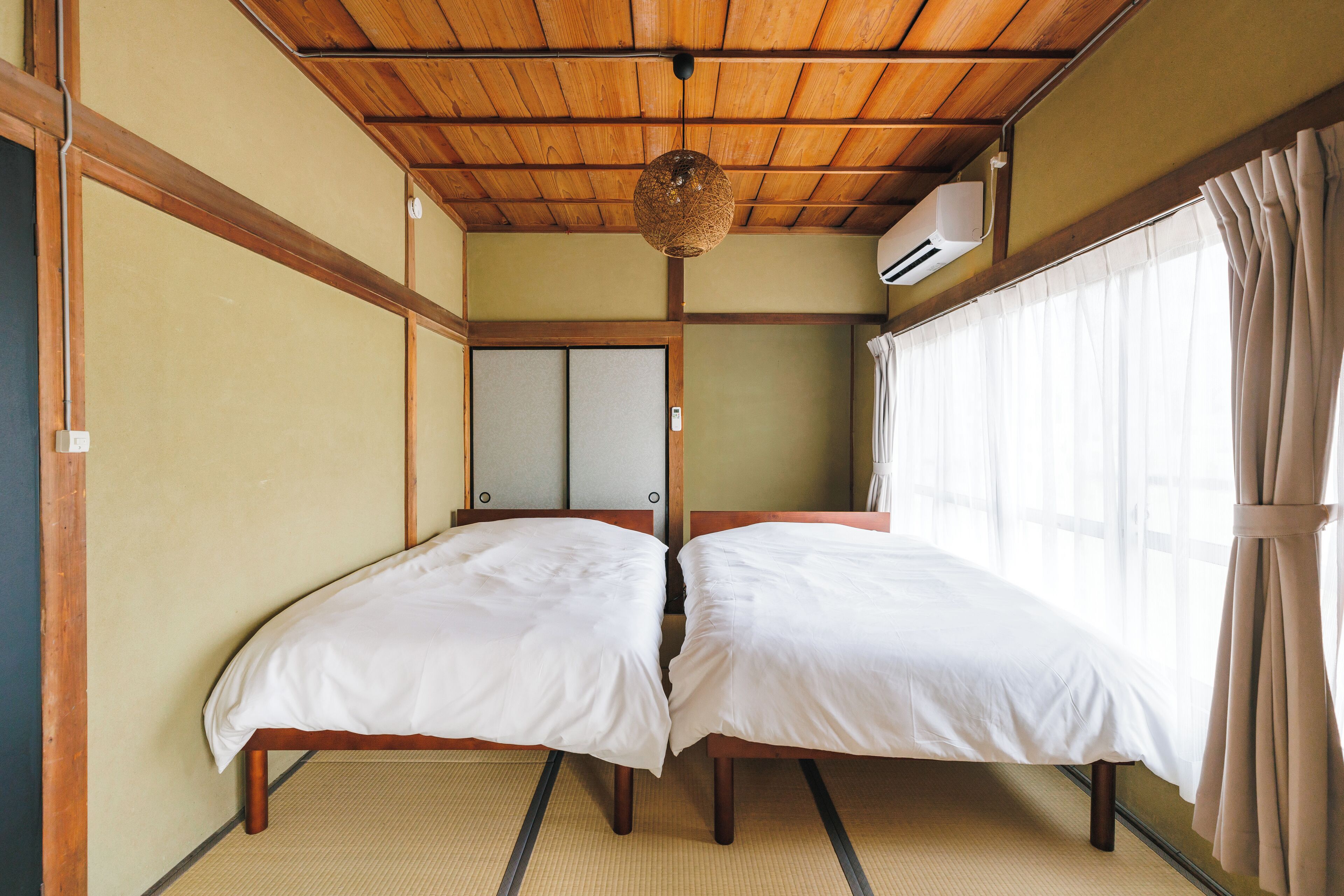 Een traditionele Japanse kamer met tatami vloerbedekking, twee bedden met witte beddengoed, een plafondventilator en een schuifdeur van shoji papier.